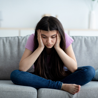 A worried young girl sitting on a sofa.